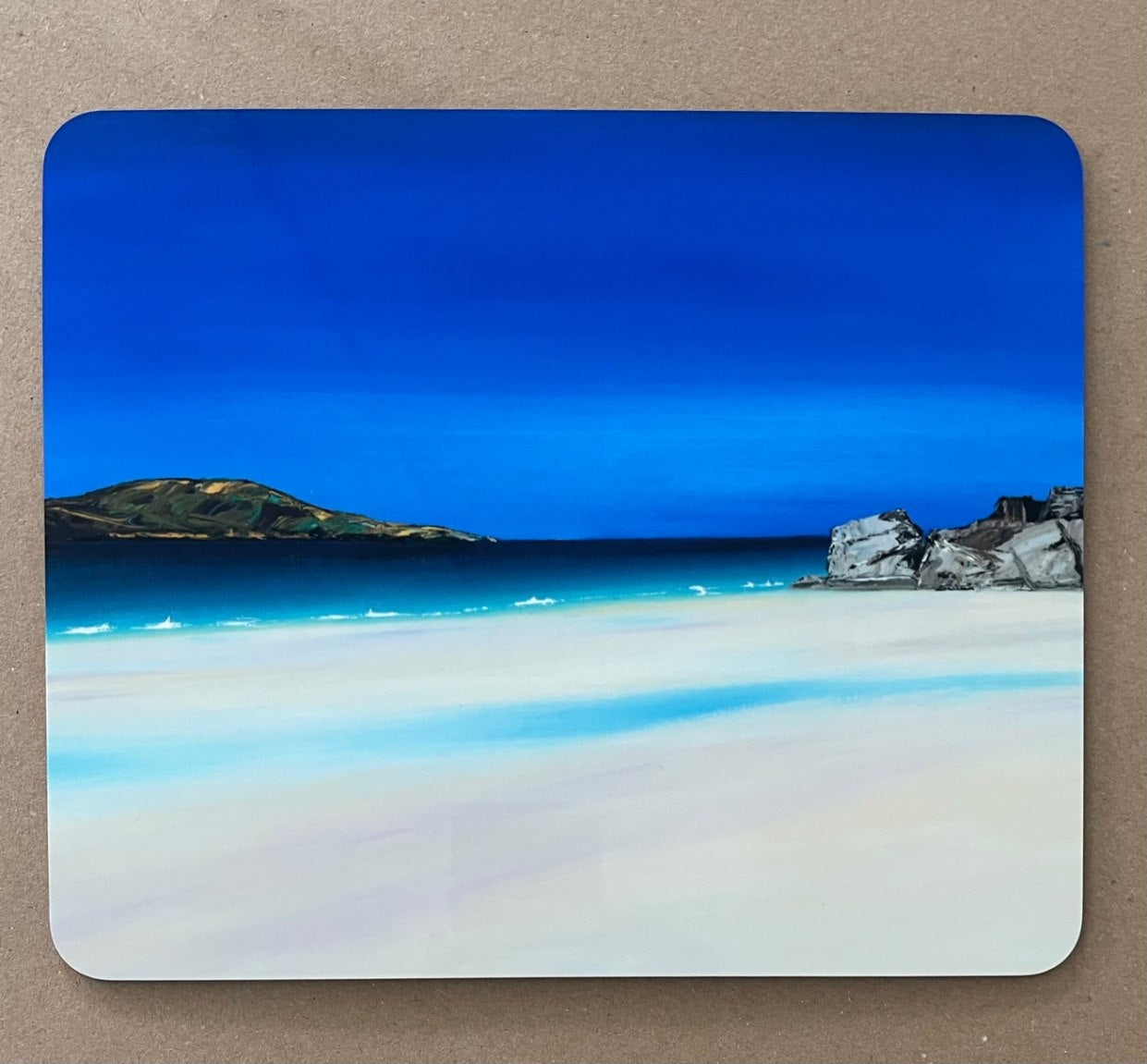 Table mat with a painting of a blue seascape and white sandy foreground.
