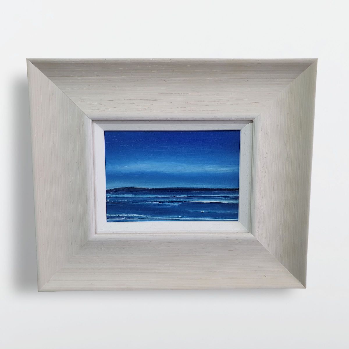 Blue Hebridean seascape oil painting set in a broad off-white frame.